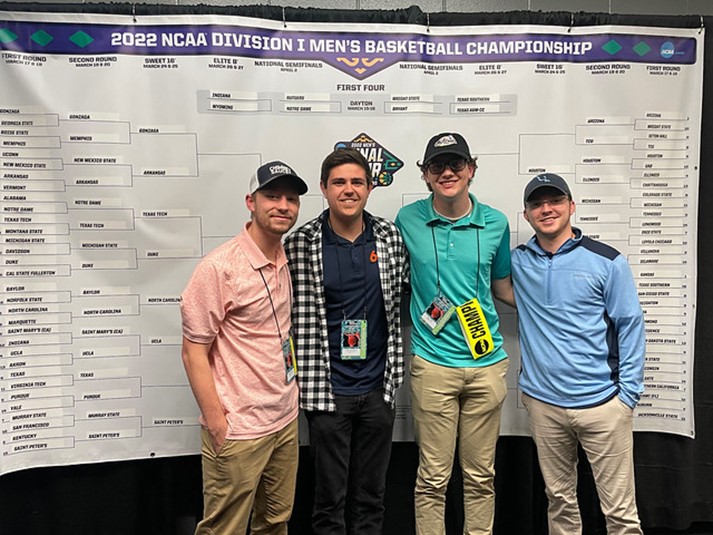 Auburn journalism students stand in front of a bracket poster at the NCAA Men's Basketball Tournament