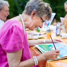 An older woman smiling as she paints with a group