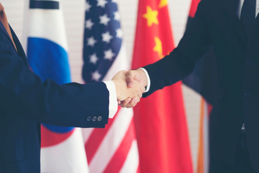 Two people shaking hands in front of several national flags
