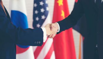 Two people shaking hands in front of several national flags