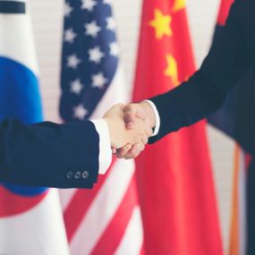 Two people shaking hands in front of several national flags