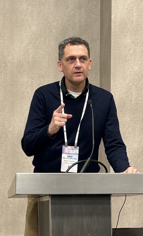Mike Milford speaking at a podium.