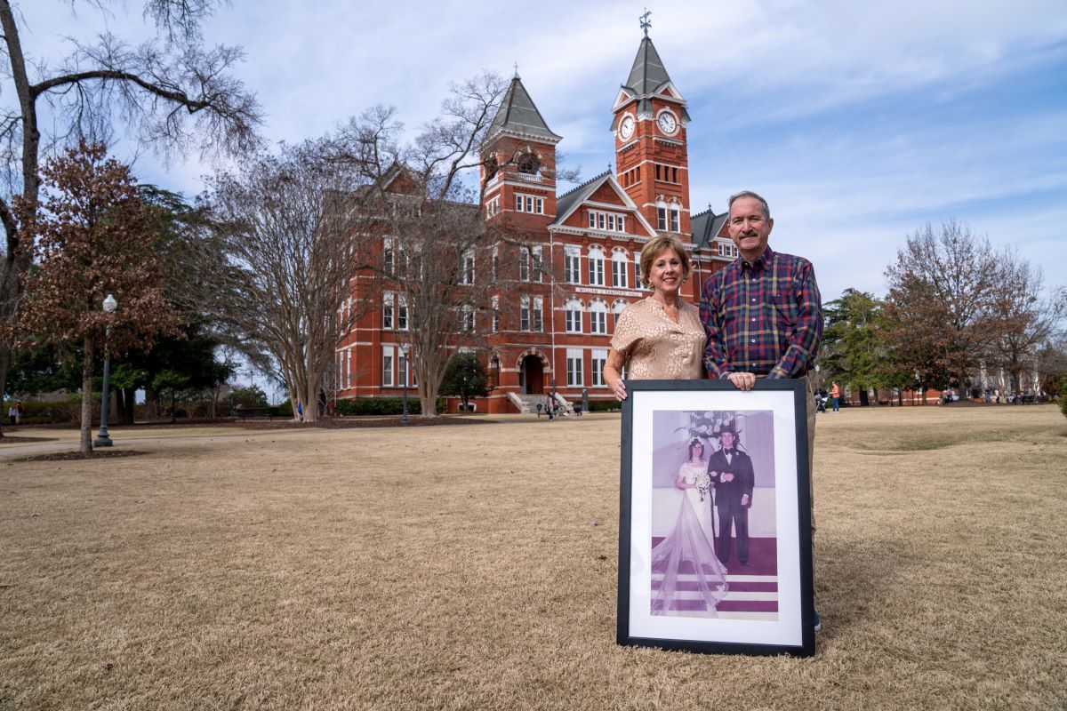 The Furlongs stand in front of Samford Hall holding a photo from their wedding