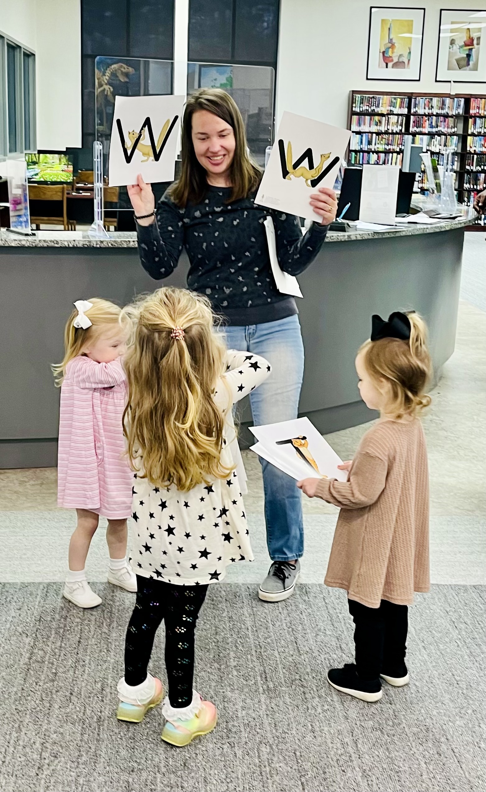 Teacher holding up letters with three children standing around her.