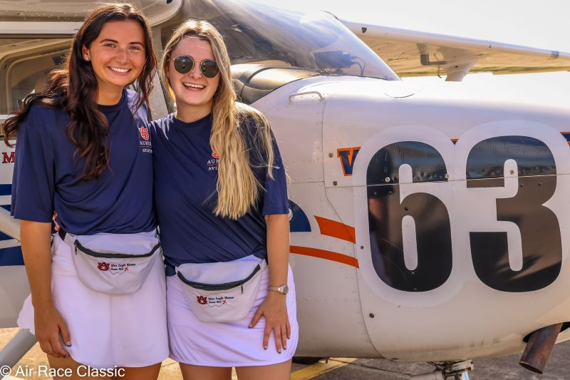 Ashley Baldwin and Meg Cooper stand in front of the Team 63 Skyhawk airplane
