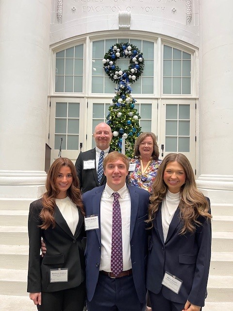 Three students and two faculty standing on stairs in front of a large glass door