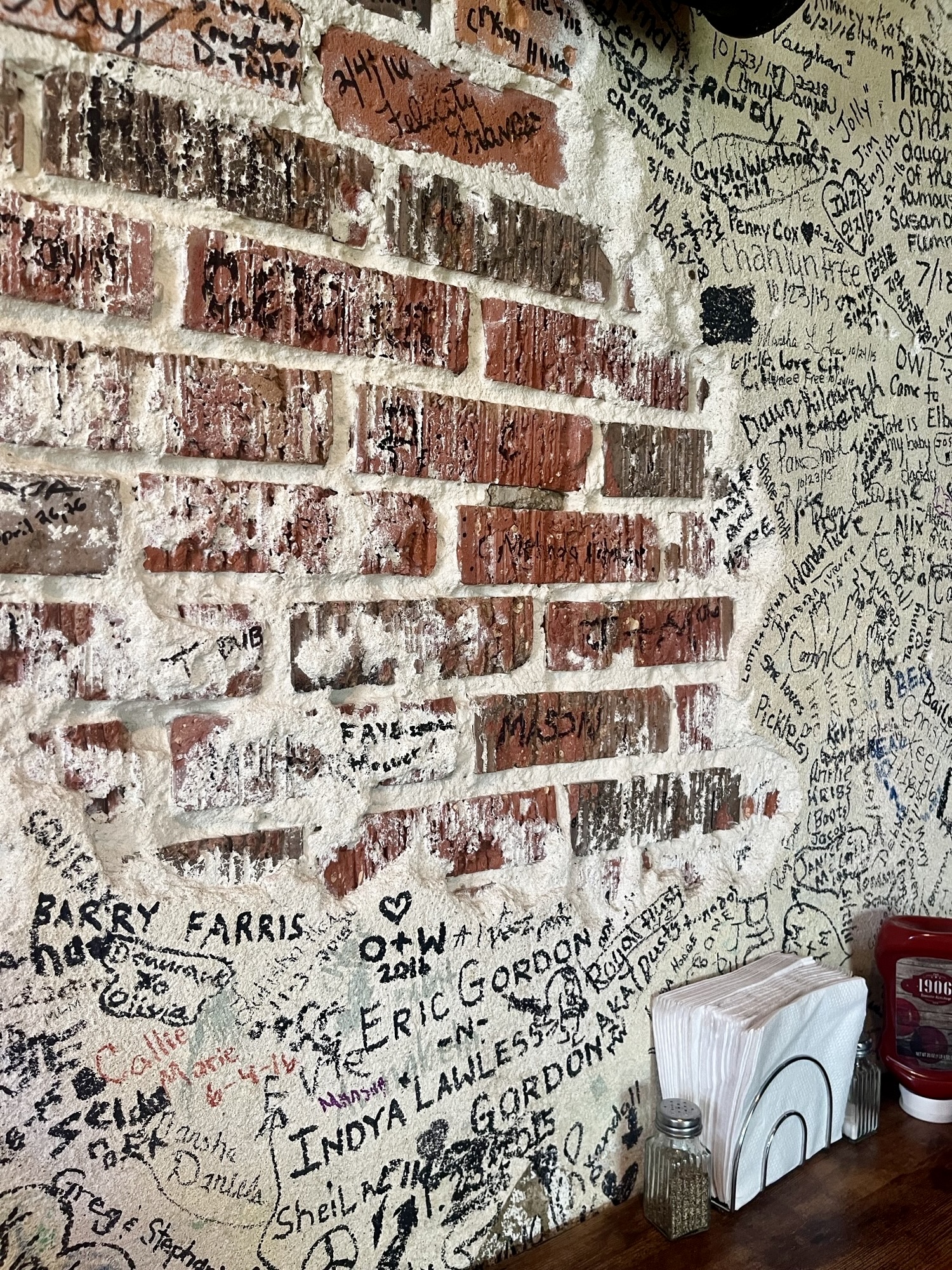 a restaurant table sits next to an exposed brick wall with messages and names written in permenant marker