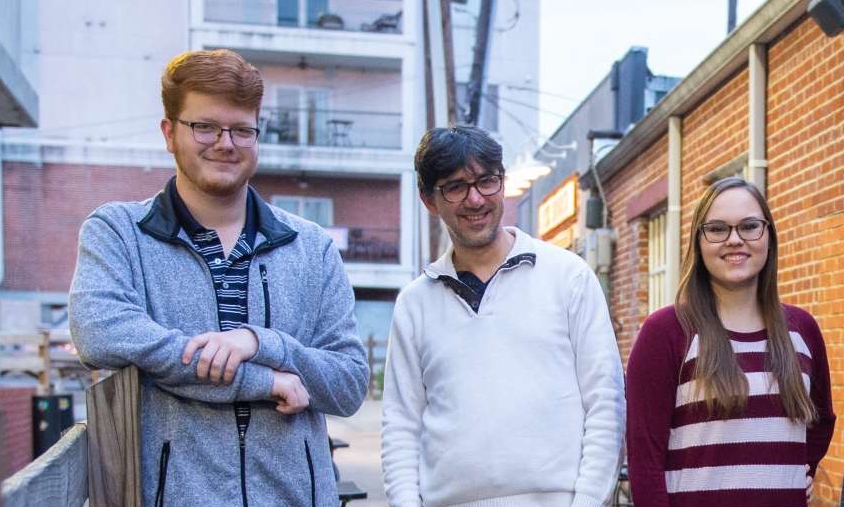 Two students standing with a professor