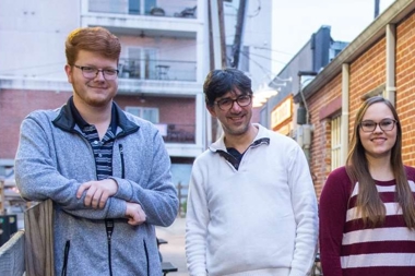 Two students standing with a professor