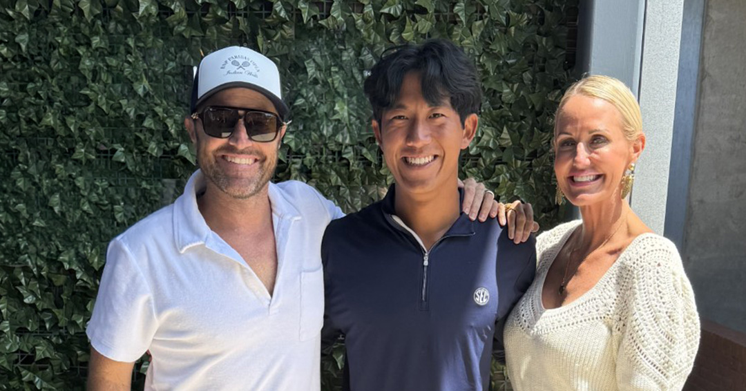 Blake and Traci pose for a photo with Nick in front of a wall of plants