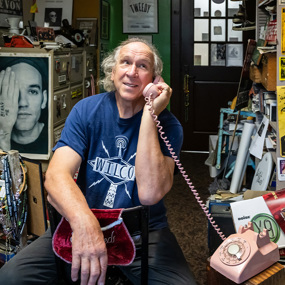 George talks on a pink rotary phone in his crowded office