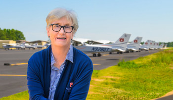 Jill Glidewell smiling for a photo on a sunny day at the Auburn airport in front of the Auburn aircraft fleet