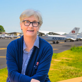 Jill Glidewell smiling for a photo on a sunny day at the Auburn airport in front of the Auburn aircraft fleet