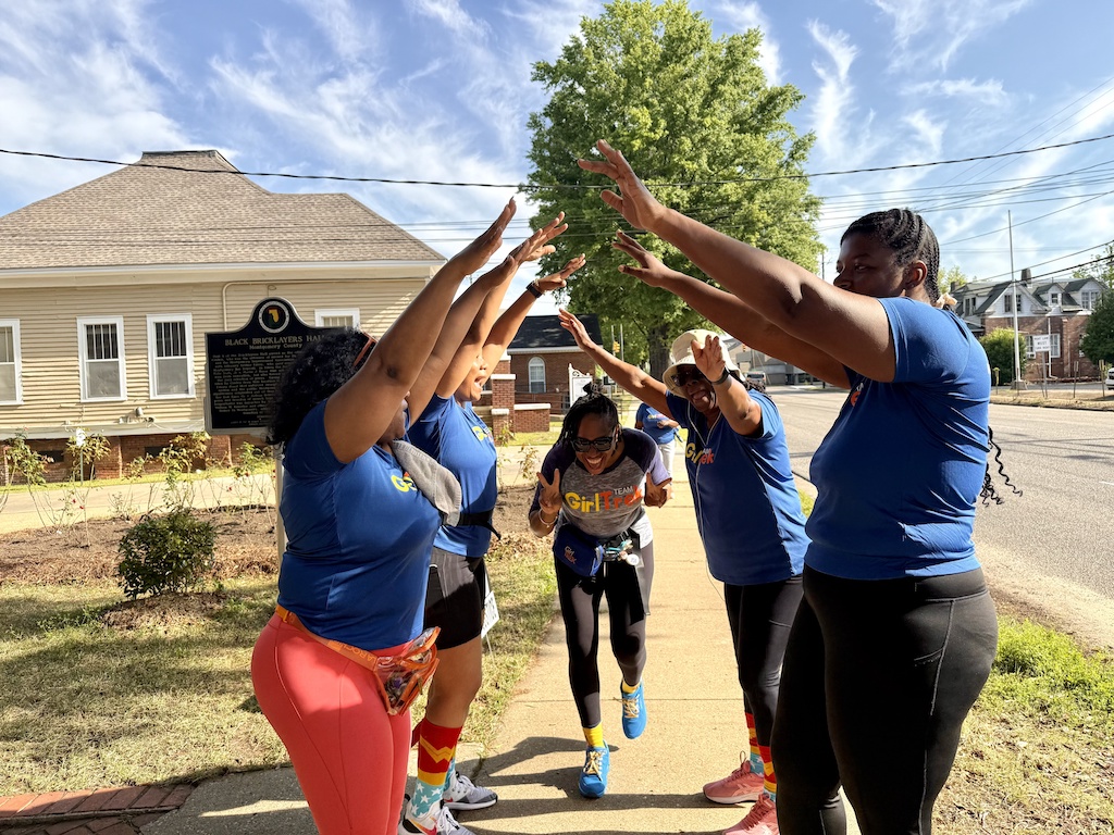 Tara Campbell dancing through a cheer tunnel formed by other GirlTrek walkers outside the Bricklayers Hall in Montgomery