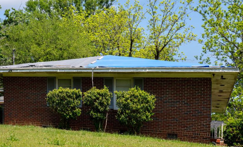 Blue tarp covering roof of a small brick house