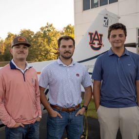 Nick Reyzin, Noah Henry and William Abbott posing for photo in front of an Auburn airplane