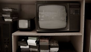 VHS tapes and recording equipment sitting on shelf beside an old television set