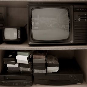VHS tapes and recording equipment sitting on shelf beside an old television set