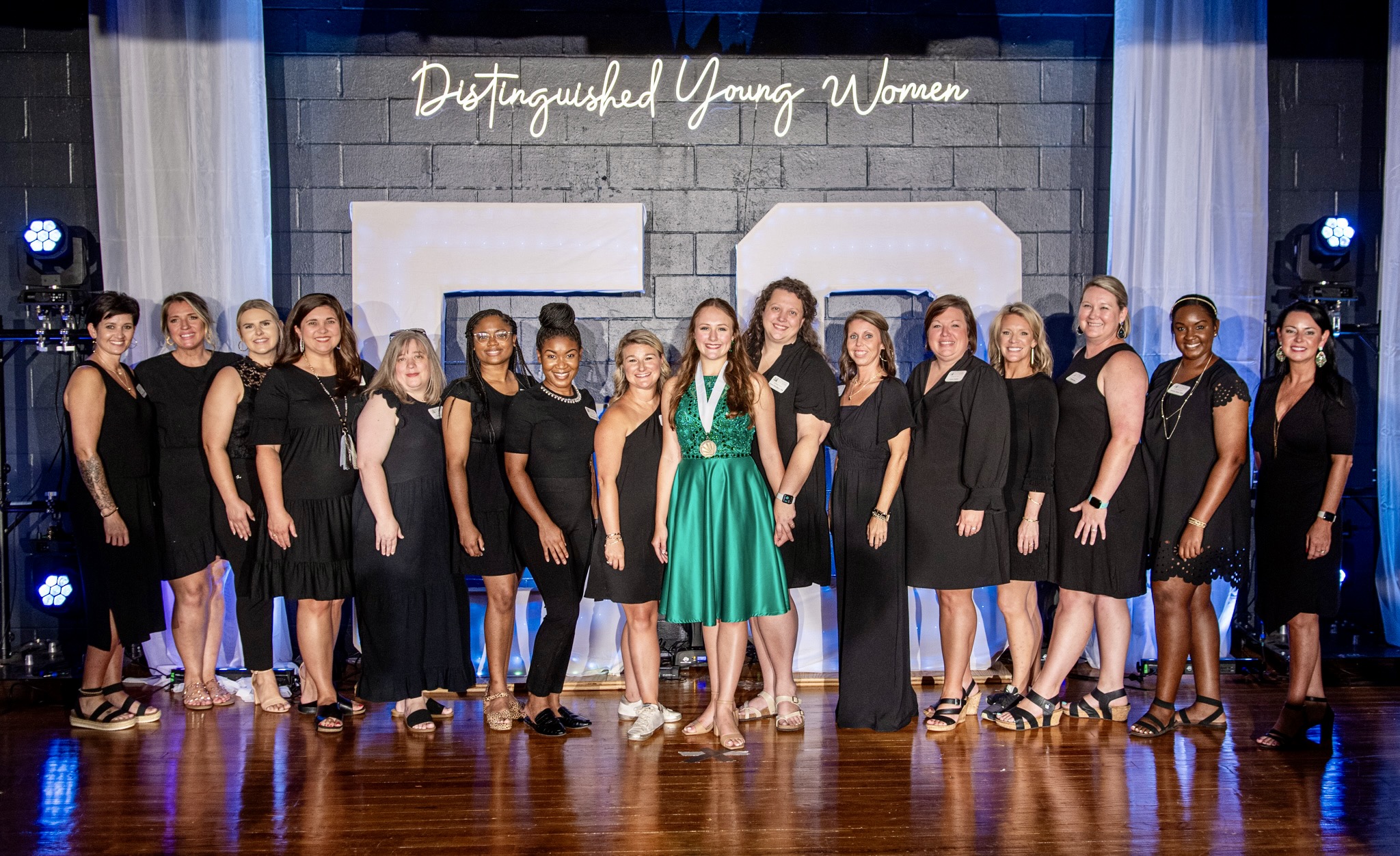 Women stand together on a stage under the banner that reads &quot;Distinguished Young Women&quot;