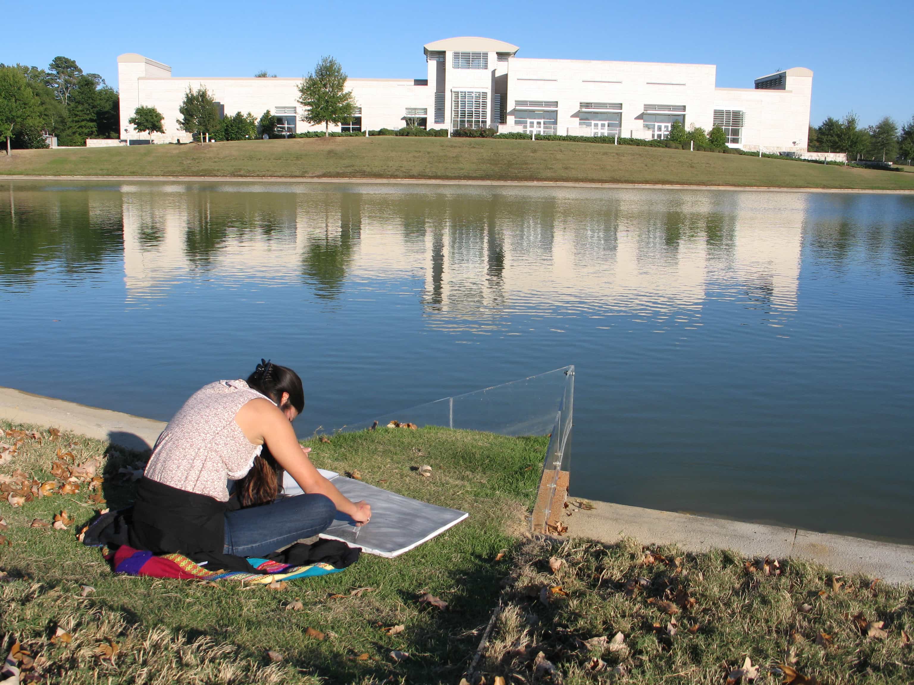 Student drawing across the lake from the Jule Collins Smith Museum of Fine Art
