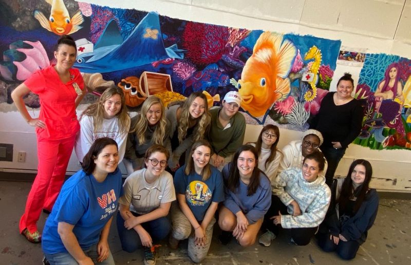 art students posed in front of colorful mural