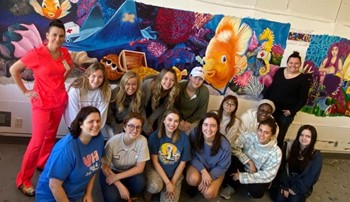 art students posed in front of colorful mural