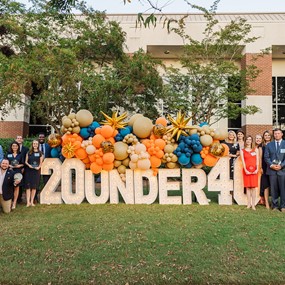 The inaugural class standing around a light-up 20 under 40 sign