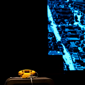 Yellow telephone sitting on stage in front of a blue background during Jitney