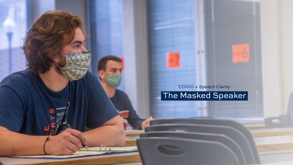 Two students wear face masks in a classroom with text reading COVID plus speech clarity, the masked speaker