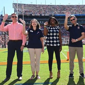College of Liberal Arts and War Eagle Productions representatives wave on the field at Jordan Hare Stadium