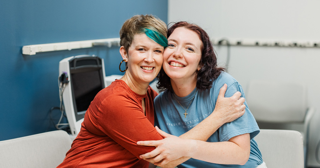 Erin and Addison sit at a table and hug