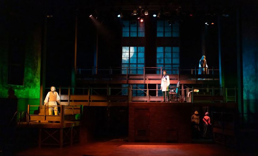 Blue and green lights illuminate specific areas of the stage and a large window projection unit shows a full moon