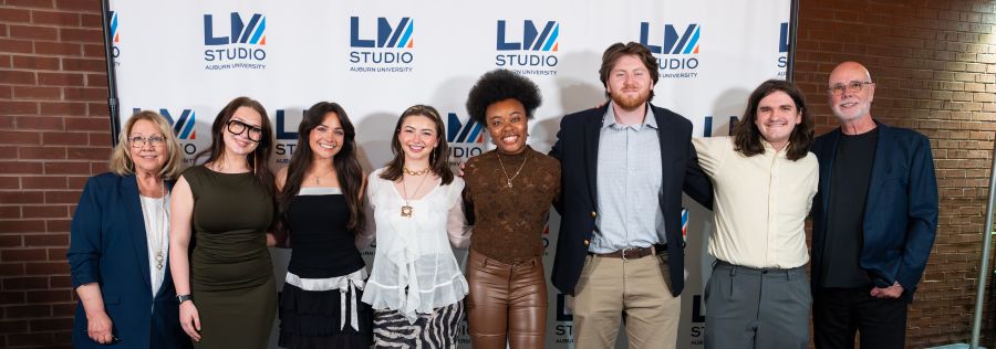 Eight people standing in front of a background with the Lucky Man Studio Logo on it
