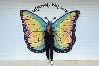 Celeste, who wears prosthetic arms, stands in front of a brick wall painted with butterfly wings